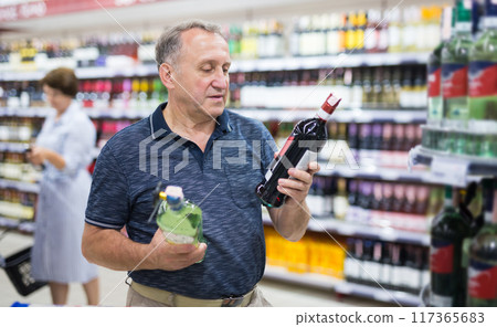 Mature man choosing alcoholic drinks in supermarket 117365683