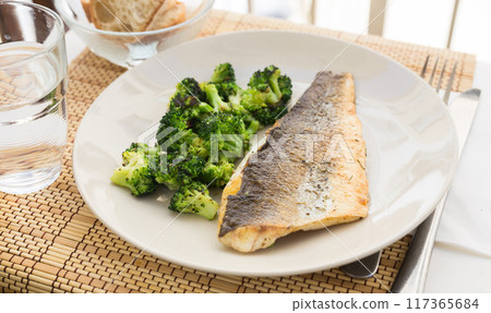Fried fillet of sea bass with garnish of broccoli on black warm stone plate 117365684