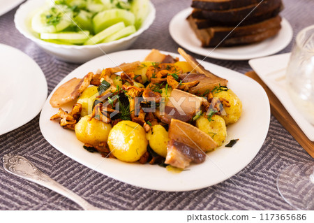 Baked potatoes with chanterelles and bacon served with herbs and lightly salted cucumbers on table 117365686