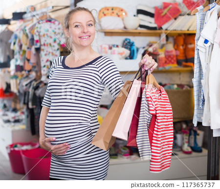 Happy pregnant woman with shopping bags in clothing shop on shopping Happy pregnant woman with shopping bags in clothing shop on shopping 117365737