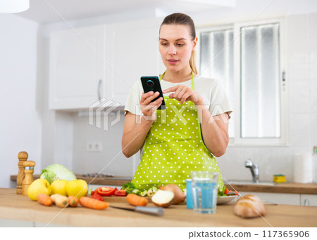 Housewife looking for recipe on internet using smart phone in the kitchen 117365906