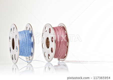 spools of blue and pink thread on a white background 117365954