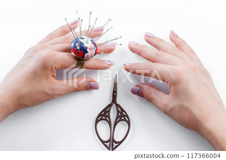 a ring with a small pillow for needles on a hand and scissors on a white background 117366004