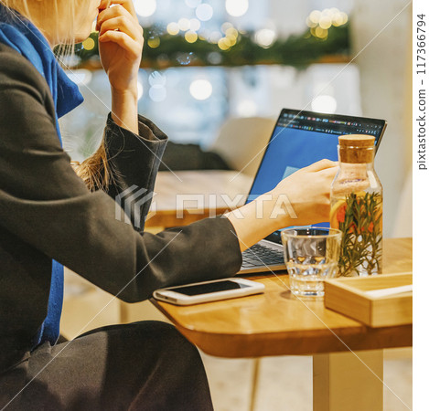 Woman working on laptop in cozy cafe, with smartphone and infused water bottle on table 117366794