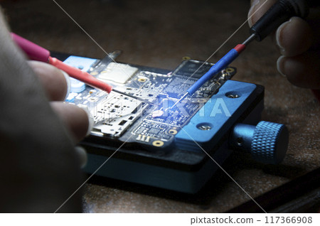 Side view of mechanic doing repairs Smartphone motherboard, smartphone repair, circuit repair 117366908