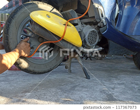 A motorcycle mechanic is adding air to a tire. 117367073