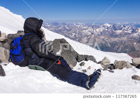 mountaineer rests sitting on a snowy slope among rocks in the highlands mountaineer rests sitting on a snowy slope among rocks in the highlands 117367265