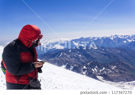 mountain climber looking at smartphone screen while standing on highland snow slope 117367270