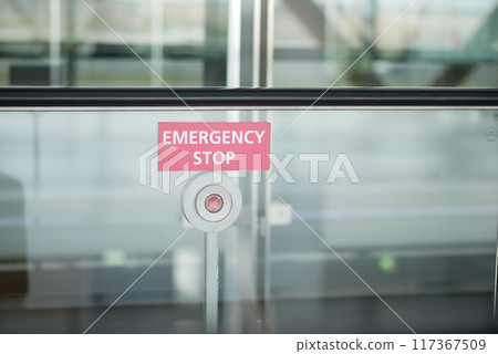 An emergency stop button is placed on a glass wall in a public space for safety measures An emergency stop button is placed on a glass wall in a public space for safety measures 117367509
