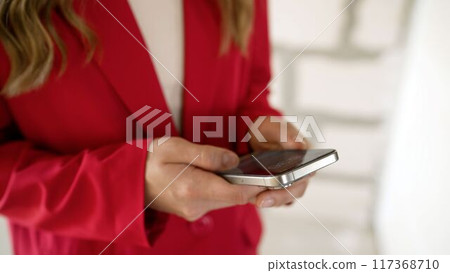 A girl writes SMS on a smartphone indoors. Girl holding a phone, close-up, searching on the phone. An unrecognizable girl holds the phone with both hands, close-up. A girl writes SMS on a smartphone indoors. Girl holding a phone, close-up, searching on the phone. An unrecognizable girl holds the phone with both hands, close-up. 117368710