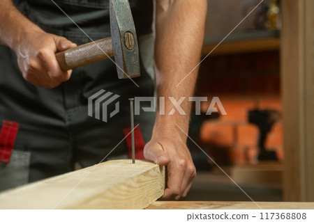 A person skillfully positions a nail against a piece of wood, preparing for a precise hammering technique. The focus is on the careful alignment needed for effective and accurate nailing as they bring 117368808