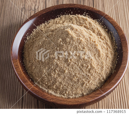 A bowl of brown powder is sitting on a wooden table 117368915