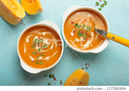 Two bowls of creamy pumpkin soup decorated with parsley and pepper on blue background top view Two bowls of creamy pumpkin soup decorated with parsley and pepper on blue background top view 117368994
