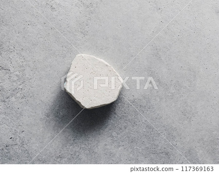 A white stone is laying on a grey surface A white stone is laying on a grey surface 117369163