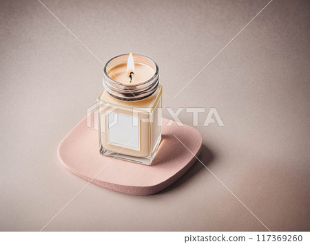 A candle is lit in a glass jar on a pink surface 117369260