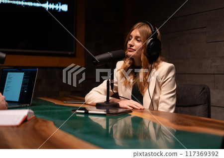 A woman is recording a podcast episode in a modern studio equipped with professional audio gear 117369392