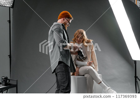 Photographer and model collaborating in a studio photoshoot, reviewing shots for a fashion project 117369393