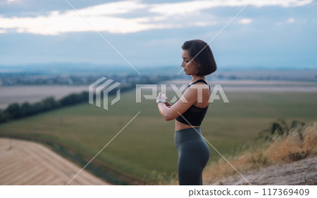 A young woman athlete is seen checking her smartwatch in a field as she works out 117369409