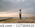 A woman peacefully enjoys a scenic sunset on a hilltop, embracing nature and finding solitude 117369410