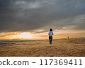A person is running in an open field during sunset with dramatic clouds in the sky 117369411