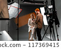 Professional Studio Photoshoot with Female Model and Photographer Adjusting Lighting 117369415
