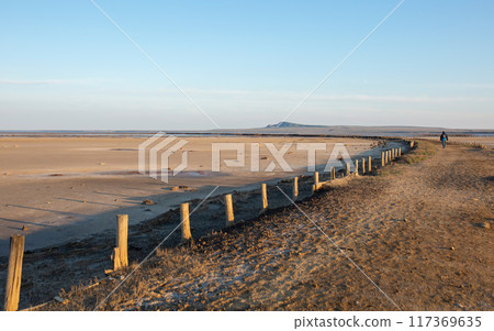 Sunset landscape with a figure walking away across the desert in the distance. Sunset landscape with a figure walking away across the desert in the distance. 117369635