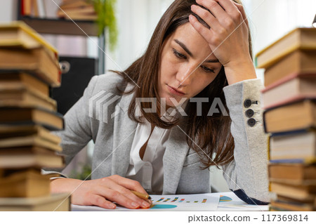 Exhausted business woman looking at documents reports stacks of books while working hard at office 117369814