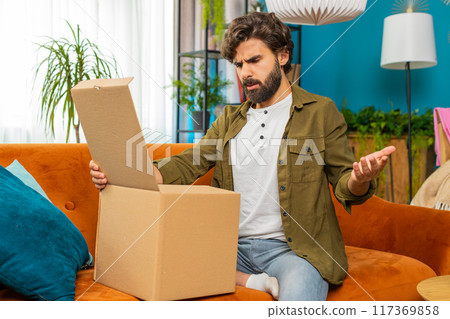 Angry dissatisfied shopper middle eastern man unpacking parcel feeling upset confused wrong delivery 117369858
