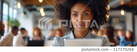 African American woman with afro hair holding a tablet while standing in front of people in the office. African American woman with afro hair holding a tablet while standing in front of people in the office. 117370268