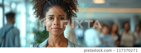 African American woman with afro hair holding a tablet while standing in front of people in the office. 117370271