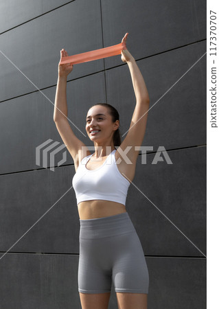 Young fit woman doing stretching for arms with fitness band 117370707