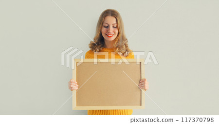 Woman decorating interior, hanging blank photo frame, wooden picture on wall in new house 117370798