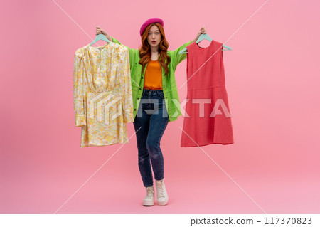 Pretty young woman in bright clothes choosing between two dresses Pretty young woman in bright clothes choosing between two dresses 117370823