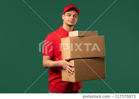 Positive postal courier man with parcel box. Happy postman delivers address package on green studio background. 117370873