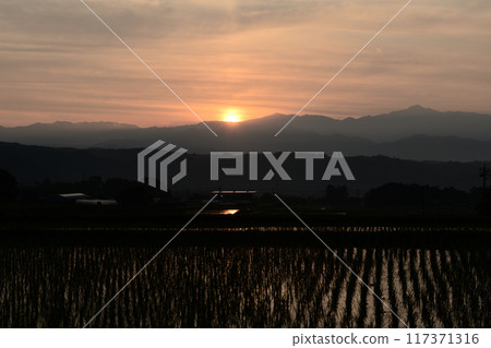 The morning sun rising over the mountains of Okuchichibu, seen from Hakushu Town in Hokuto City, paints the sky and rice fields crimson red. The morning sun rising over the mountains of Okuchichibu, seen from Hakushu Town in Hokuto City, paints the sky and rice fields crimson red. 117371316