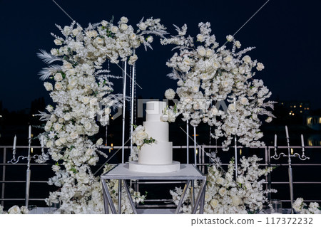 Wedding setup with three-tier white cake with floral accents. Wedding inspiration, luxury events Wedding setup with three-tier white cake with floral accents. Wedding inspiration, luxury events 117372232