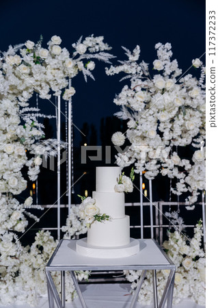 Wedding setup with three-tier white cake with floral accents. Wedding inspiration, luxury events Wedding setup with three-tier white cake with floral accents. Wedding inspiration, luxury events 117372233