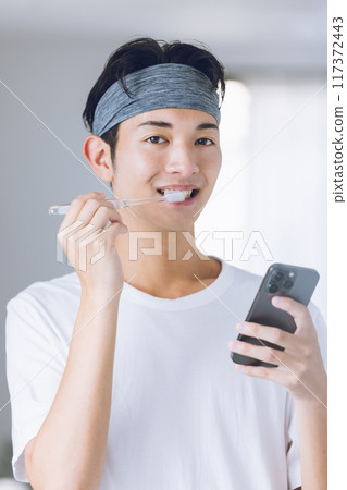 年輕人一邊刷牙一邊看智慧型手機 117372443