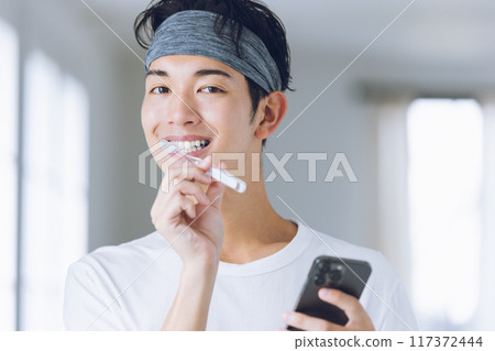Smiling young man brushing his teeth 117372444