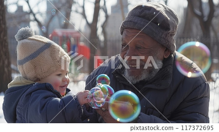 Joyful african american elderly man plays with grandchild and colorful bubbles outdoors in sunlight 117372695