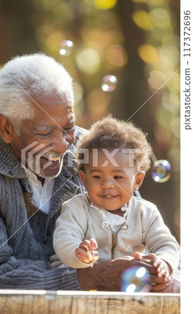 Joyful african american elderly man plays with grandchild and colorful bubbles outdoors in sunlight Joyful african american elderly man plays with grandchild and colorful bubbles outdoors in sunlight 117372696