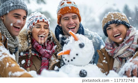 Joyful group of friends creating a snowman in a picturesque snowy park on a delightful winter day 117372748