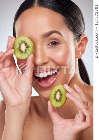 Kiwi makes for a nourishing booster to your skincare routine. Studio portrait of a beautiful young woman posing with kiwi against a grey background. 117372881