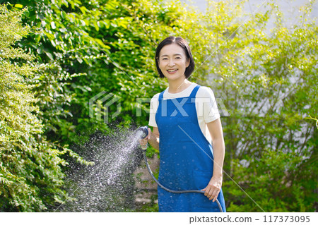 微笑的中年婦女在花園裡的綠樹澆水 微笑的中年婦女在花園裡的綠樹澆水 117373095