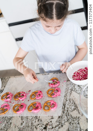 With focused attention, this budding culinary artist dips pretzels into a pot of melted chocolate, creating sweet delights in the warmth of a well-lit home kitchen. With focused attention, this budding culinary artist dips pretzels into a pot of melted chocolate, creating sweet delights in the warmth of a well-lit home kitchen. 117373404