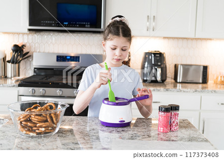 With focused attention, this budding culinary artist dips pretzels into a pot of melted chocolate, creating sweet delights in the warmth of a well-lit home kitchen. With focused attention, this budding culinary artist dips pretzels into a pot of melted chocolate, creating sweet delights in the warmth of a well-lit home kitchen. 117373408
