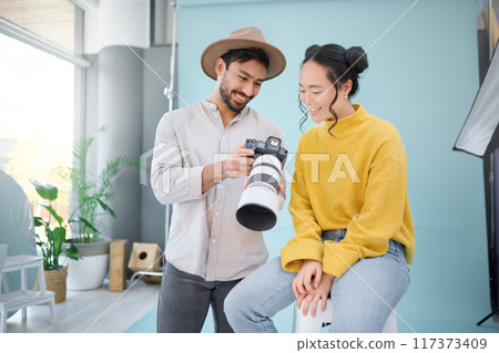 Creative, photographer and model choosing a picture on the camera from the photoshoot in the studio. Photography, creativity and cameraman talking to a woman for the best image on a artistic set. 117373409