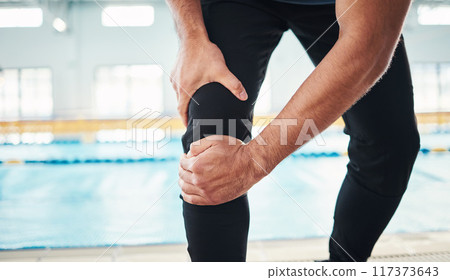 Hands, knee injury and swimming instructor holding his joint in pain with a pool in the background of a gym. Fitness, coach and anatomy with a sports man suffering from a sore leg during exercise Hands, knee injury and swimming instructor holding his joint in pain with a pool in the background of a gym. Fitness, coach and anatomy with a sports man suffering from a sore leg during exercise 117373643