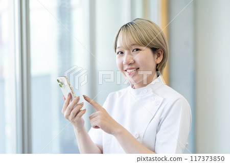 A young blonde short-haired chiropractor holding a smartphone (free hair color, work in your own way, work environment) 117373850