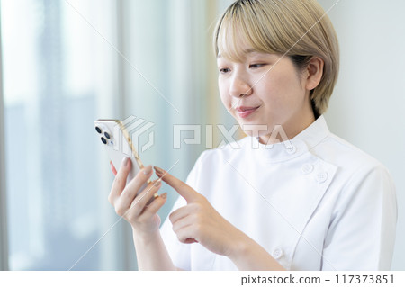 A young blonde short-haired chiropractor holding a smartphone (free hair color, work in your own way, work environment) A young blonde short-haired chiropractor holding a smartphone (free hair color, work in your own way, work environment) 117373851